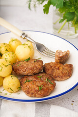 Plate with cutlets, boiled baby potatoes and dill on white grunge table in kitchen