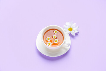 Cup of natural chamomile tea with flower on lilac background