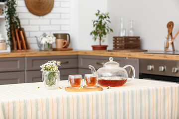 Fototapeta na wymiar Wooden tray with teapot, cups of natural chamomile tea and flowers on table in kitchen