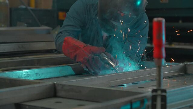 Man in mask works with welding metal structures at factory. Creative. Welder in equipment works at industrial plant. Worker with welding and welding sparks from metal