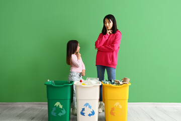 Thoughtful Asian mother with her little daughter and recycle bins near green wall