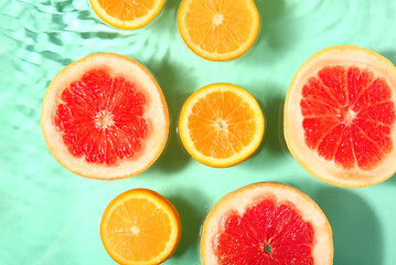 Slices of fresh orange and grapefruit in water on turquoise background
