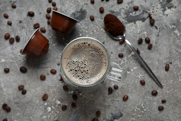 Cup of delicious coffee, pods and beans on grey grunge table