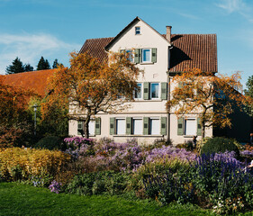 Fototapeta na wymiar House with nice garden in fall. Flowers in the City Park of Bietigheim-Bissingen, Baden-Wuerttemberg, Germany, Europe. Autumn Park and house, nobody, bush and grenery