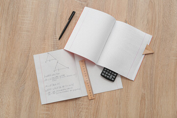 Open copybooks with math formulas, ruler and calculator on wooden table
