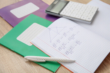 Open copybook with formulas, calculator and pen on wooden table