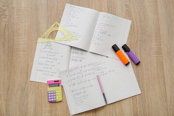 Open copybooks with math formulas and stationery on wooden table