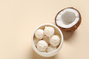 Bowl with delicious white chocolate candies and coconut on beige background