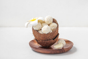 Coconut shell with white chocolate candies and plumeria flower on light table