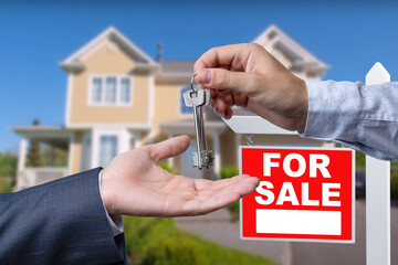 Real Estate Agent Handing Over the House Keys in Front of a Beautiful New Home and For Sale Real Estate Sign.