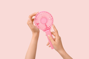 Hands of young woman with mini fan on pink background