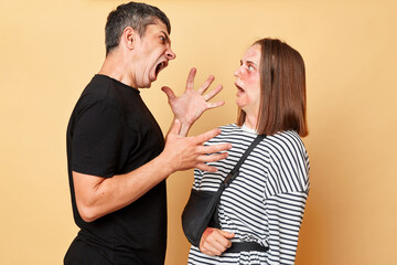 Aggressive violent screaming man and injured woman with bruise isolated over beige background...