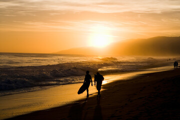 Naklejka premium orange sunset on beach with couple walking silhouette