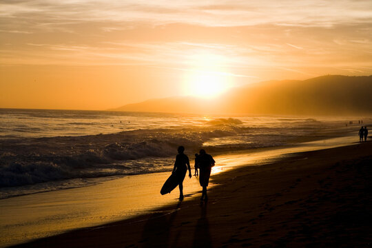 orange sunset on beach with couple walking silhouette