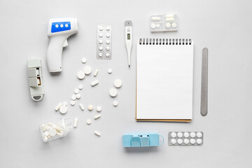 Composition with pills, thermometer, stethoscope and notebook on grey background