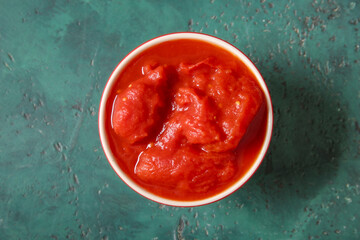 Bowl of canned tomatoes on color background