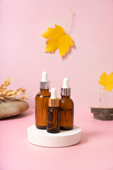 Glass dropper bottles with cosmetics oil or serum at autumn scene composition with podium
