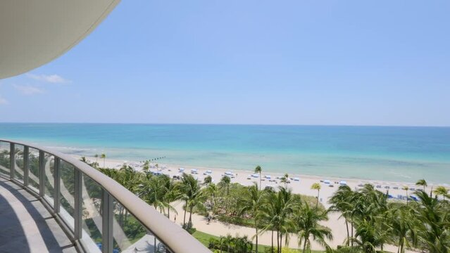 Long summer terrace with comfy lounge chairs and tables in multi-storey hotel complex in Sunny Isles Beach. Stunning scenery on waterfront with white sand and palm trees