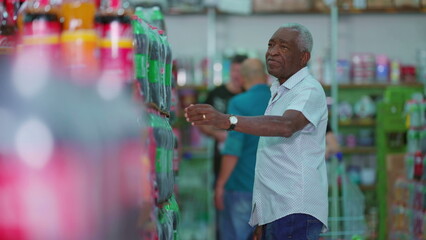 African American older shopper at supermarket searching for product to buy at soda shelf aisle