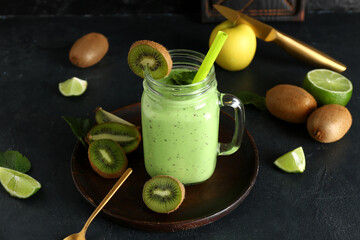 Mason jar of fresh kiwi smoothie with mint and lime on black background
