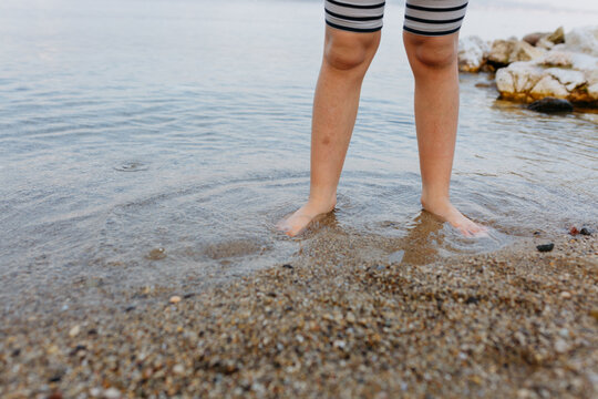 barefeet child legs standing in the water in stone beach
