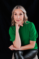 Confident blonde business woman sitting against black background