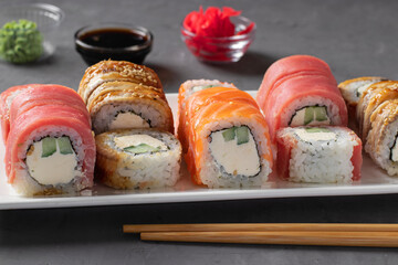 Rolls set with salmon, tuna and smoked eel with philadelphia cheese on white plate on gray background. Served with soy sauce, wasabi, pickled ginger and chopstick