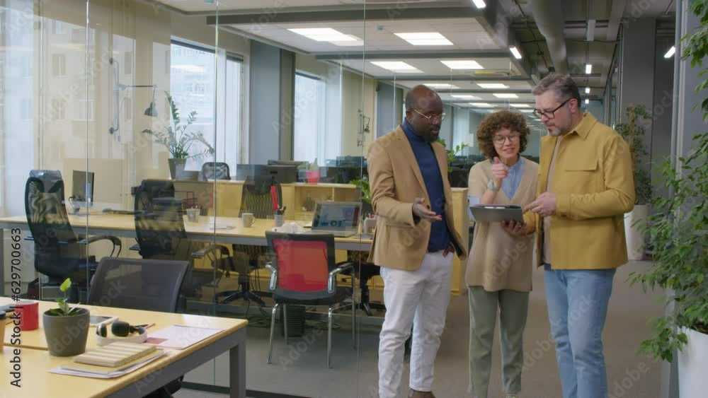 Poster full shot of three multiethnic coworkers standing in office looking at folder with documents and arg