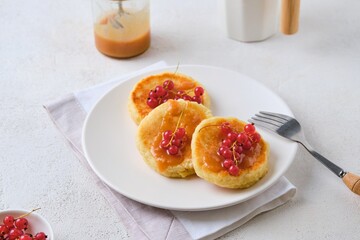 Breakfast, portioned cheesecakes with salted caramel and red currants on a white plate on a light concrete background.