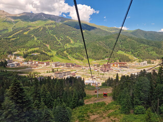 The cable car on an aerial tram rises with a view of the mountains and green coniferous forest in the background in summer. Arkhyz, Karachay-Cherkessia, Russia
