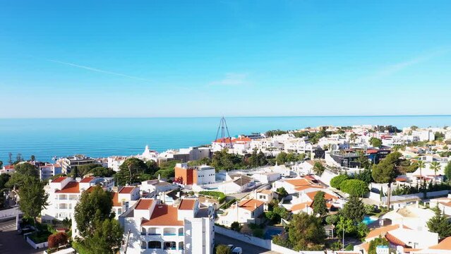 Aerial footage of the beautiful town of Albufeira in Portugal, showing the Praia de Albufeira and Praia da Oura Beach in the background, on a clear sunny blue sky day in the summer time.