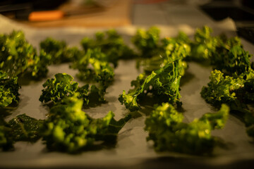 Prepared kale for frying fries, kale leaves arranged on a baking sheet before putting in the oven during a magical sunset in the kitchen - obrazy, fototapety, plakaty