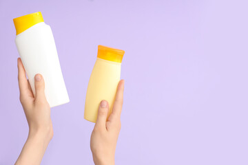 Female hands with bottles of sunscreen cream on lilac background