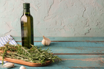 Board with fresh rosemary, garlic and bottle of olive oil on color wooden table