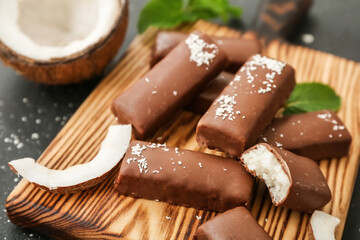 Wooden board with tasty chocolate covered coconut candies on black background