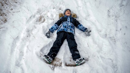 Fototapeta na wymiar Little boy having fun in snow lying and making snow angel. People playing outdoors, winter holidays and vacation, active leisure.