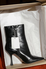 Black leather ankle boots with pointed toe and high heels with blank price tag, product photography 
