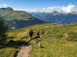 Fototapeta na wymiar Trail running group runs down above Davos Klosters in the direction of Lake Davos. Running in the mountains. Beautiful trailrun landscape in Switzerland. High quality photo