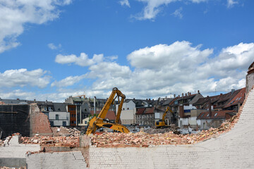 Several construction excavators are engaged in dismantling an old house. Dismantling the city's housing stock for renovation