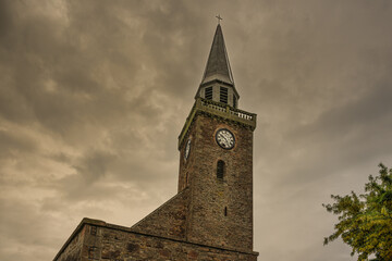 2023-06-11 A OLD BRICK CLOCK TOWER IN INVERNESS SCOTLAND WITH A DARK STORMY SKY AND A GREEN TREE FROM A ABSTRACT UPWARD ANGLE