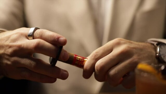 Close-up male hands with a finger are cutting a cigar with a guillotine of scissors on a table