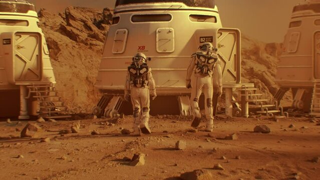 Two astronauts in spacesuits walk toward research station, colony or scientific base on Mars. Manned exploring space mission on red planet. Futuristic colonization and space exploration concept.