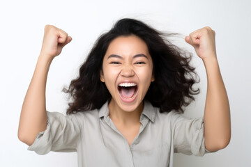 Asian woman with fists raised, showing relief, happiness, and excitement. She is against a white wall, wearing a bright jacket. Joy and enthusiasm can be seen in her eyes.
