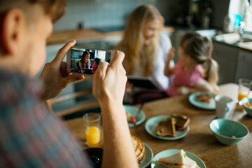 Young family taking a picture with their smart phone while having breakfast in the kitchen in the morning