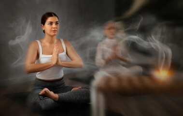 Portrait of sporty smiling young girl sitting in Padmasana yoga position with her arms in namaste...