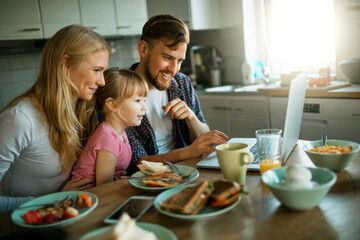 Young family having breakfast in the morning and using a laptop
