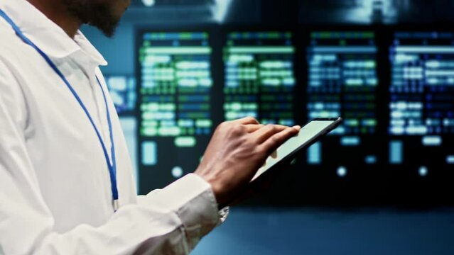 Skilled worker walking through supercomputers delivering web content to online customers. Repairman in server room using tablet to make sure critical systems are working errorless, close up