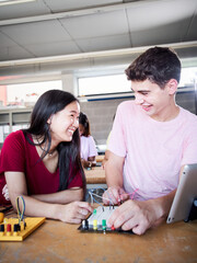 Fototapeta premium Vertical multiracial boy and girl students at a technical high school look at each other smiling in class. Classmates collaborating on a high school project: programming electric robots in the lab.