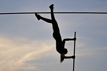 A female pole vaulter (silhouette) jumping with a beautiful sky in the background. Track and field athlete. Young woman pole-vaulting. Pole vault competition