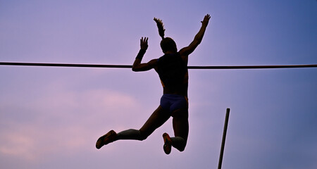 A female pole vaulter (silhouette) jumping with a beautiful sky in the background. Track and field athlete. Young woman pole-vaulting. Pole vault competition - obrazy, fototapety, plakaty